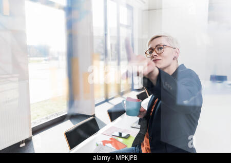 Confident businesswoman looking at glass pane in office Stock Photo