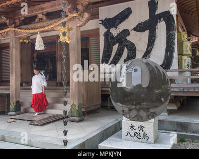 Woman in traditional shinto costme at Haiden,  Hall of Worship.  Yatagarasu, three-legged crow symbol, on stone disc.  Kumano Hongu Taisha, Wakayama P Stock Photo