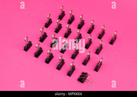 binder clips arrayed standing up in minimalist pattern on colorful pink magenta background Stock Photo