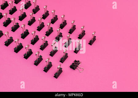 binder clips arrayed standing up in minimalist pattern on colorful pink magenta background Stock Photo