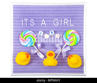 Purple display board with white letters spelling It's a Girl, blocks spelling baby, surrounded by swirled colorful lollipops and yellow rubber duckies Stock Photo