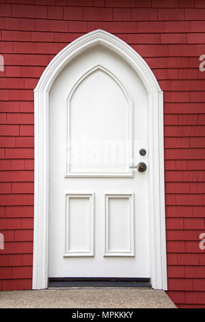 White fancy door outside with a red wood siding wall background, concrete walkway sidewalk. Stock Photo