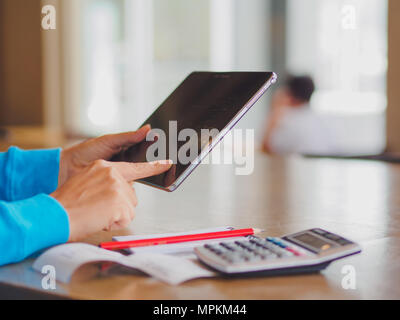 Pretty Young womans hands holding and using tablet for online shopping, bill, pencil and calculator on the table. Online payment. Female working on ta Stock Photo
