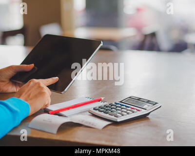 Pretty Young womans hands holding and using tablet for online shopping, bill, pencil and calculator on the table. Online payment. Female working on ta Stock Photo