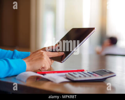 Pretty Young womans hands holding and using tablet for online shopping, bill, pencil and calculator on the table. Online payment. Female working on ta Stock Photo