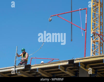 A building construction worker wearing a safety harness attached to an Alsina Fall Arrest System, England, UK Stock Photo