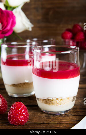 Raspberry dessert from whipped white chocolate mousse, raspberry puree as jelly, and base from almond cookies, rustic wooden background Stock Photo