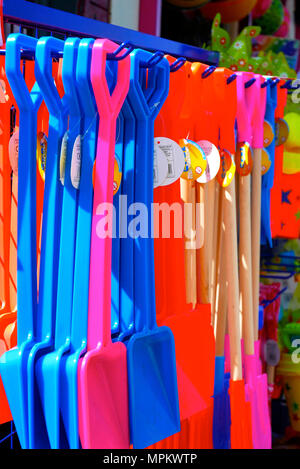 Colourful childrens' plastic beach spades hanging from rack for sale outside seaside shop,Blackpool,Lancashire,UK Stock Photo