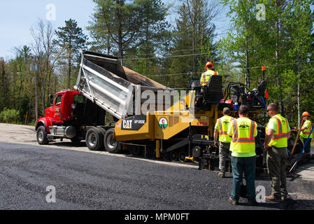 A dump truck and road paver laying asphalt on a parking lot in Speculator, NY USA Stock Photo