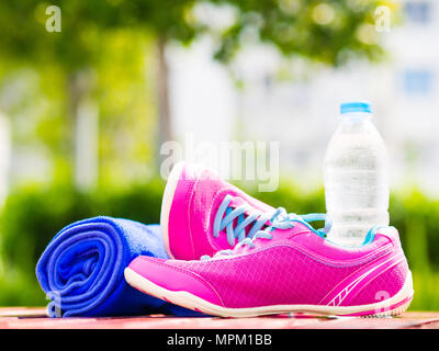 Pair of pink sport shoes towel water bottle on wooden board. In the background forest or park trail. Accessories for running sport. Stock Photo