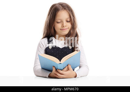 Little girl seated at a table reading a book isolated on white background Stock Photo