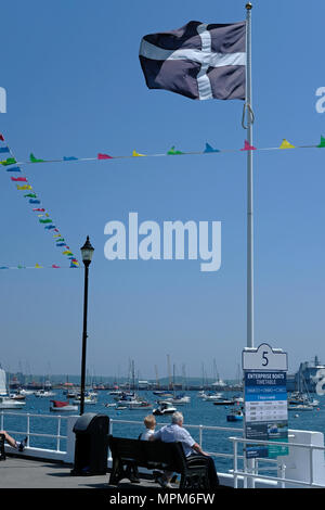 A retired couple sit in the sun in Falmouth, Cornwall under the Cornish flag. St Piran's. Stock Photo