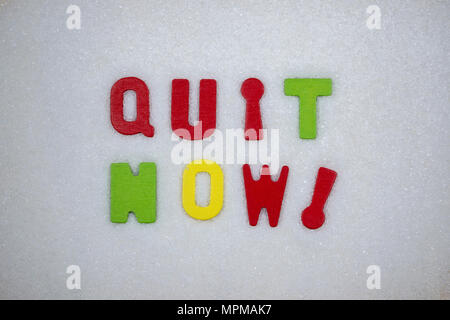 'Quit now!' Colorful text and letters in wood on white sugar crystals background Stock Photo