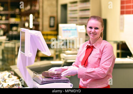 young saleswoman at the fresh counter in the supermarket - sale of cheese and meat Stock Photo