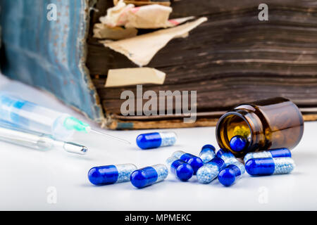 Bunch of blue pills with glass ampoules, injection, thermometer and old medical book. Stock Photo