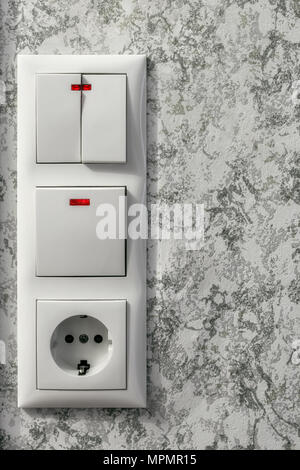 Electric block with a socket and light switches on a wall background with motley wallpaper. Stock Photo