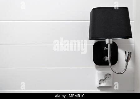 Black wall lamp with a socket on the background of the white wall in the interior of the room. Stock Photo