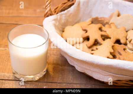 Basket with gingerbreads of different shapes next to glass of milk on wooden surface Stock Photo