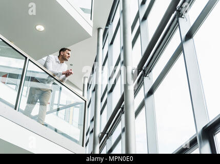 Businessman in office building leaning on railing Stock Photo