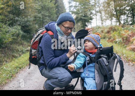 Son eating bread, sitting in his back-basket, next to his mother during hiking Stock Photo