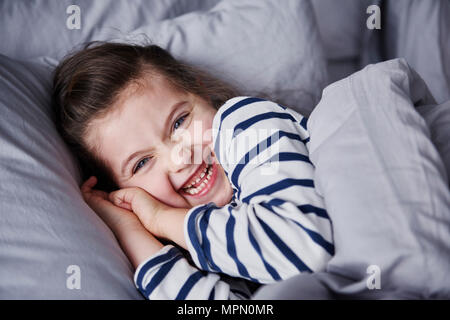 Portrait of laughing little girl lying in bed Stock Photo