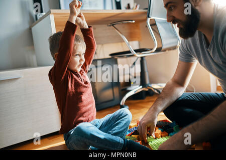 Father and son sitting on the floor at home playing together with building bricks Stock Photo