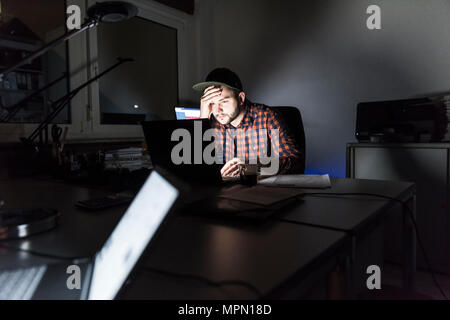 Portrait of freelancer sitting at desk working on laptop at night Stock Photo