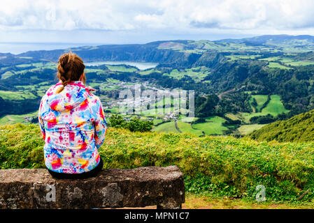 Azores, Sao Miguel, Woman sitting on stone bench looking towards the city and lake Furnas Stock Photo