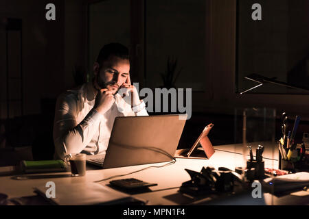 Pensive businessman working on laptop in office at night Stock Photo