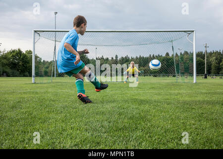 Young football player kicking ball in front of goal with goalkeeper Stock Photo