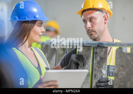 Woman with tablet talking to man with ladder on construction site Stock Photo