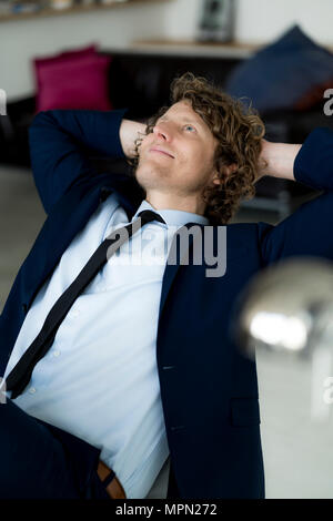Relaxed businessman sitting in office with hands behind head Stock Photo