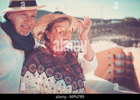 Senior couple in a rooftop stay together looking at the panorama over the city. Vintage filter for a retro look. Both with hats. Stock Photo