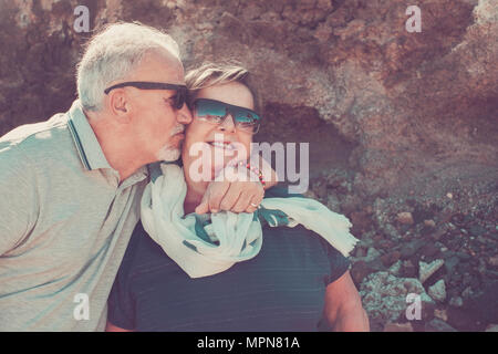 Happy elderly couple on vacation in Tenerife with white hair and sunglasses smile and kiss each other on the cheek Stock Photo