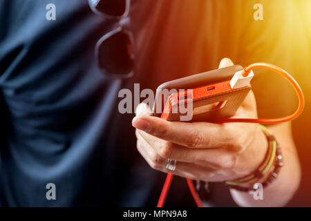 Man in black tshirt charging his smartphone with power bank, power unit. Focus on person hand and diveses. Stock Photo