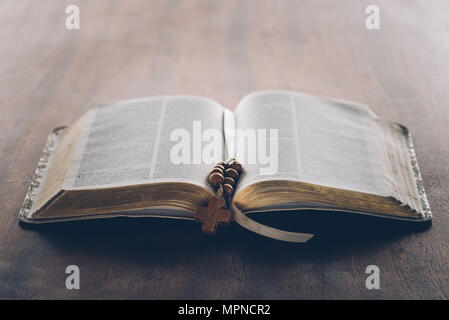 open holy bible and rosary with cross on wooden table Stock Photo