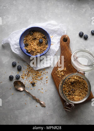 Homemade granola in a glass jar and in a bowl with fresh blueberries on a gray background Stock Photo