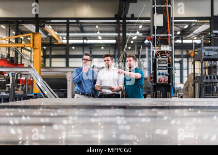Three men sharing tablet on factory shop floor Stock Photo