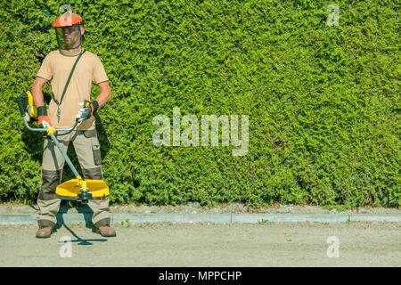 Gas String Trimmers Work. Caucasian Garden Worker with Power Tool. Stock Photo