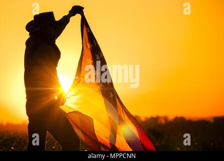 Men Western Wearing Celebrating Independence Day Waving Large American Flag During Scenic Sunset Vista. United States of America Patriot in Cowboy Hat Stock Photo
