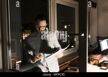 Businessman in office at night using smartphone Stock Photo