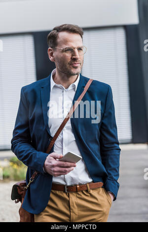 Confident businessman standing outdoors with smartphone Stock Photo