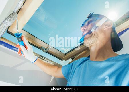 Room Painter Multitasking. Caucasian Construction Worker with Paint Brush in His Mouth Painting Walls Using Roller. Stock Photo