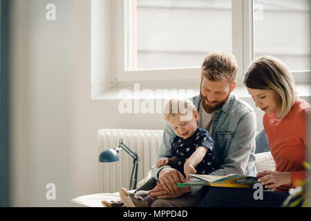 Little boy sittiing on father's lap, mother reading out children's book Stock Photo