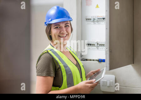 Portrait of smiling female electrician with tablet at fusebox Stock Photo