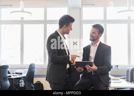 Two businessmen standing in office, discussing solutions, using digital tablet Stock Photo