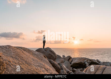 Italy, Sardinia, man standing on rock at sunset looking at view Stock Photo