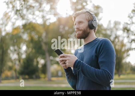 Man listening music with headphones   and smartphone in a park Stock Photo