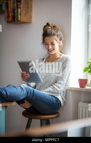 Smiling woman sitting on stool using tablet Stock Photo