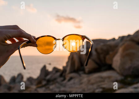 Man's hand holding sunglasses in front of evening sun, close-up Stock Photo